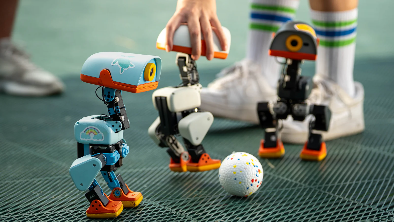 Three Microducks in different colours playing with a ball on a sports court