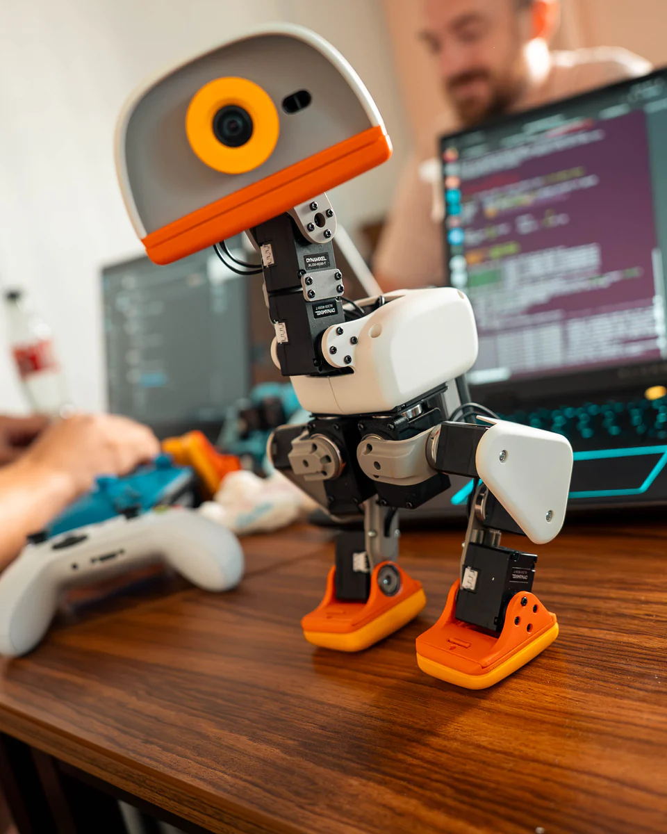 A Microduck standing on a desk beside a developer coding on a laptop
