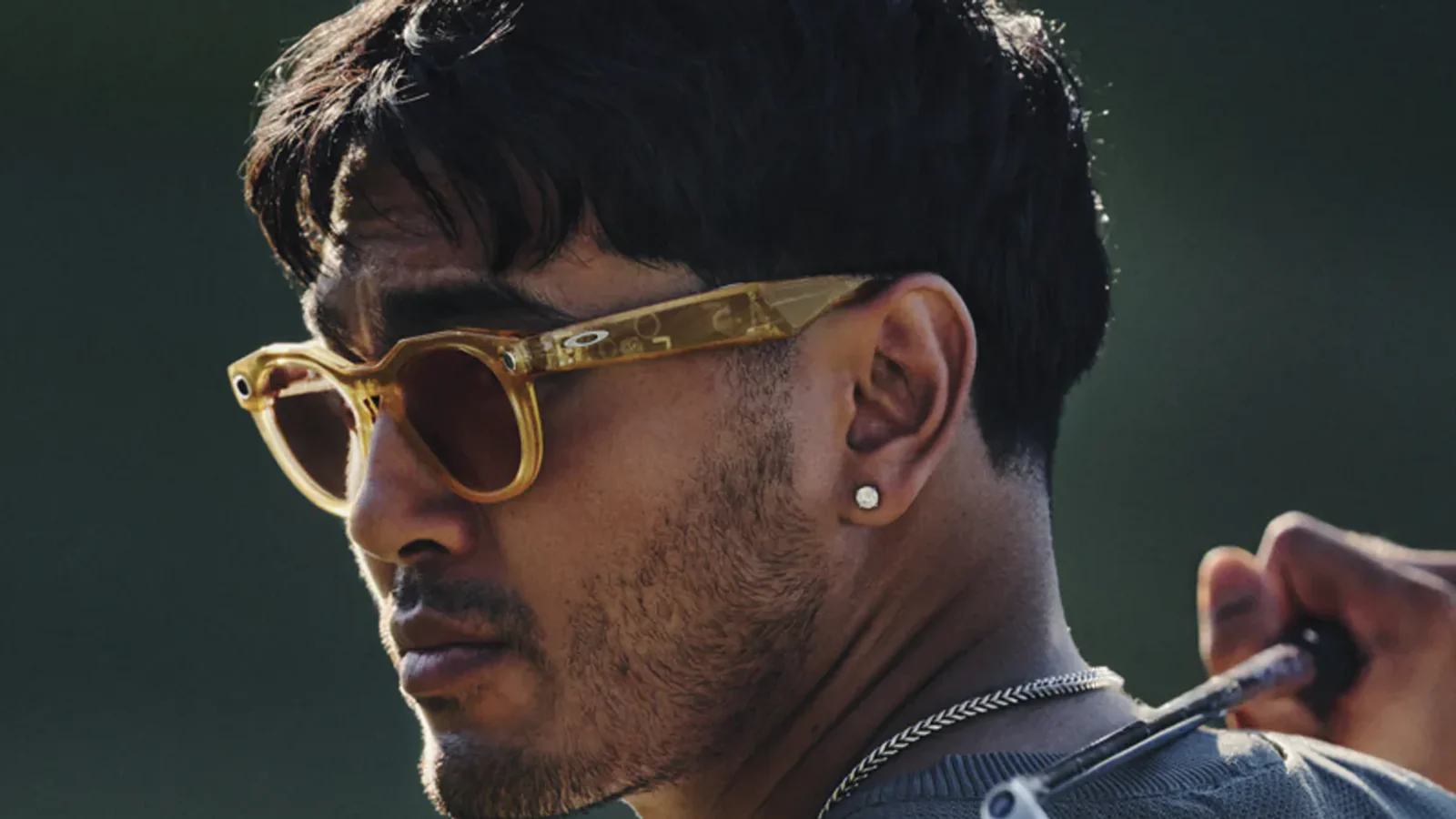 A man wearing translucent amber Oakley Meta HSTN smart glasses, seen in profile