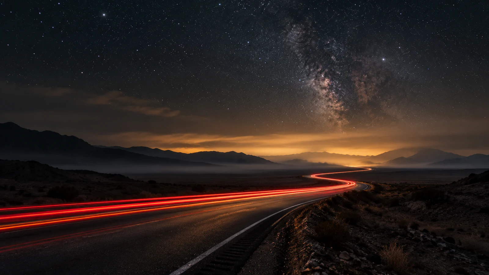 Red tail-light trails curving along an empty desert highway under a starry night sky